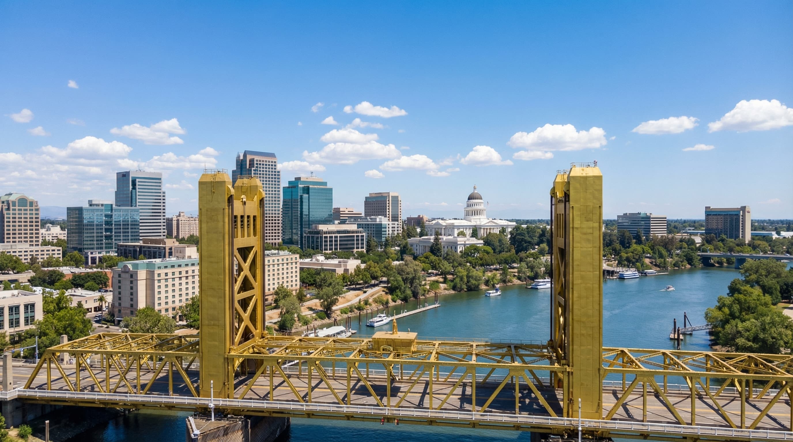 Aerial view of Sacramento California skyline from Tower Bridge with iconic golden bridge in foreground, Sacramento River, State Capitol dome, and clear blue sky